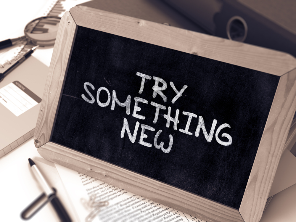 Try Something New - Inspirational Quote Handwritten on Chalkboard. Composition with Small Chalkboard on Background of Working Table with Ring Binders, Office Supplies, Reports. Blurred, Toned Image.